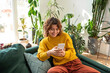 © Westend61 - Smiling young woman using smart phone sitting on couch