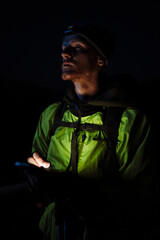 Young tourist man wearing hiking equipment using cellphone at night