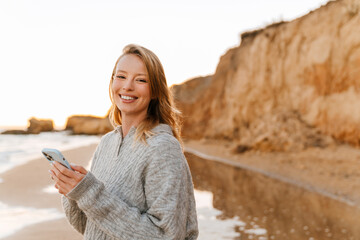 Beautiful smiling woman using smartphone during walk at beach