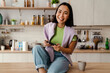 © Drobot Dean - Excited asian woman playing online game on mobile phone while sitting in kitchen