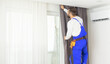 © Angelov - Young man installing curtains over window.