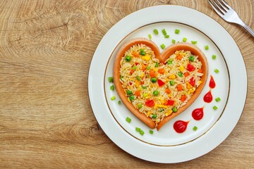 Wall Mural - Fried rice with carrots,onions,tomatoes,green peas,spring onions,eggs and soy sauce in heart shaped sausage on plate with wooden background.Healthy food idea for Valentine's day.Top view.Copy space