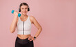 © Picture Store - Cheerful young woman in headphones wearing sportswear doing sport exercise. Fitness concept. Attractive happy lady in headphones wearing sportswear and standing over pink backdrop