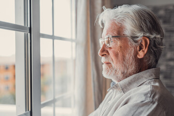 Pensive elderly mature senior man in eyeglasses looking in distance out of window, thinking of personal problems. Lost in thoughts elderly middle aged grandfather suffering from loneliness, copy space