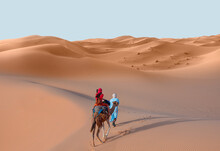 A Woman In A Red Turban Riding A Camel Across The Thin Sand Dunes Of The In Western Sahara Desert, Morocco, Africa