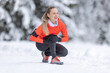 A young fit woman holds a reinforced knee after straining her cruciate ligament during cross-country training in the snow during the winter season