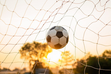 Wall Mural - A ball in goal net for street soccer football under the sunset ray light. Film picture style.