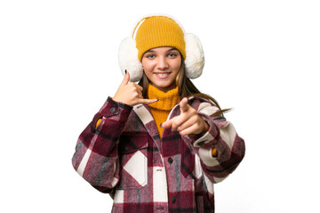 Poster - Teenager caucasian girl wearing winter muffs over isolated background making phone gesture and pointing front