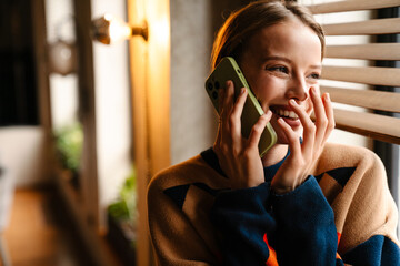 Wall Mural - Beautiful woman laughing while talking on cellphone standing near window