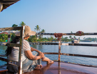 Attractive and Happy woman or lady with hat enjoys her tropical vacation on backwater of alleppey or Alappuzha from Houseboat. Selective focus on subject and background blur. Copy space