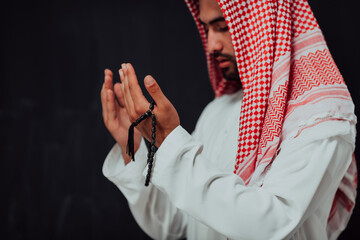 Wall Mural - Arabian man in traditional clothes making traditional prayer to God, keeps hands in praying gesture in front of black chalkboard representing modern islam fashion and ramadan kareem concept