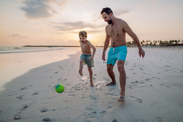 Wall Mural - Father with his son plaing football on the beach.