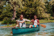 © .shock - Couple adventurous explorer friends are canoeing in a wild river surrounded by the beautiful nature
