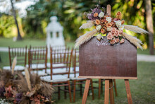 A Welcome Board Sign With A Beautiful Flower And Rustic Decoration, Standing In Front Of Wedding Entrance.