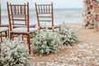 Wedding wooden chairs decorated with flowers. Rustic aisle chairs standing on sand for ceremony on the beach. Natural, shabby, boho wedding decor