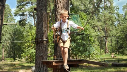 Wall Mural - Boy holding by rope while walking on cable between two trees. Active childhood, healthy lifestyle, kids playing outdoors, children in nature