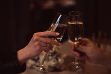 Two Glasses With Sparkling Champagne Wine In Hands, Concept For Holiday, Bokeh, In A Restaurant. Romantic Dinner. Man And Woman Are Holding Glasses Of Champagne. Concept For Valentine's Day Or Date