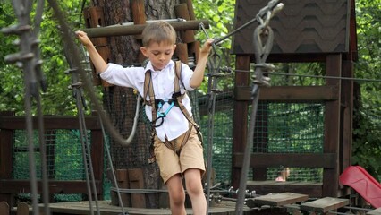 Wall Mural - Cute boy having fun while walking on wobbly rope bridge at adventure park. Active childhood, healthy lifestyle, kids playing outdoors, children in nature.