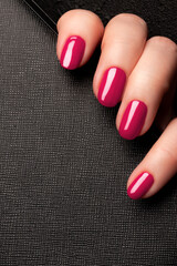 Wall Mural - Female hand with beautiful manicure - viva magenta, pink nails on black leather surface background. Nail care concept