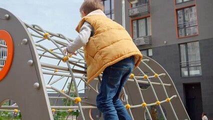 Wall Mural - Little boy climbing up on the rope net at public children playground in the yard. Active child, sports and development, kids playing outdoors.