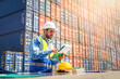 © nuttawutnuy - Engineer wears PPE checking container storage with cargo container background at sunset. Logistics global import or export shipping industrial concept.