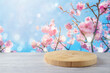 Empty wooden log on wooden table over cherry blossom flowers background. Spring and Easter mock up for design and product display