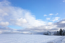 White Barn In A Snowy Northern Maine Landscape With A Windmill And A Variety Of Clouds From An Incoming Weather System.