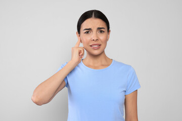 Sticker - Young woman suffering from ear pain on light grey background