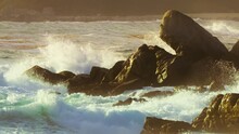 Slow Motion Seascape Background Footage Of Rocky Coast On West Coast California USA. Stormy Pacific Ocean Waves Breaking On Sharp Wet Sea Cliffs Rocks With White Splashes On Cinematic Golden Sunset 4K