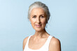 Portrait of an senior woman with perfect skin and natural makeup in a white tank top on a blue background