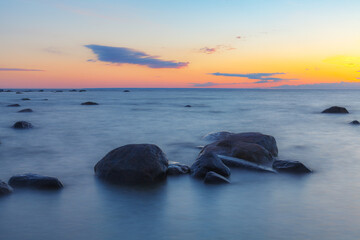 Wall Mural - A beautiful scene of sunset sky reflecting on water with boulders of Baltic sea shore