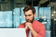 © Liubomir - Serious thinking businessman close up, man in red casual shirt working inside modern office, mature boss working with laptop at workplace while sitting