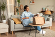 © Prostock-studio - Happy young pregnant black lady unpacking box and holding cup, touching belly and smiling, sitting on sofa at home