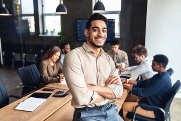 Successful person. Confident arab businessman leaning on desk in office, posing with folded arms and smiling at camera