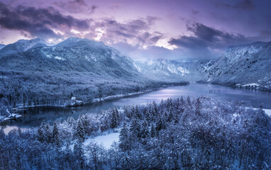 Aerial drone view of beautiful winter landscape with lake, snowy forest and mountains at sunset top view, Slovenia