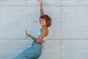 Wall Mural - latin african american woman smiling happy and excited in the street with mobile phone