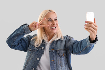 Canvas Print - Mature blonde woman with mobile phone taking selfie on light background