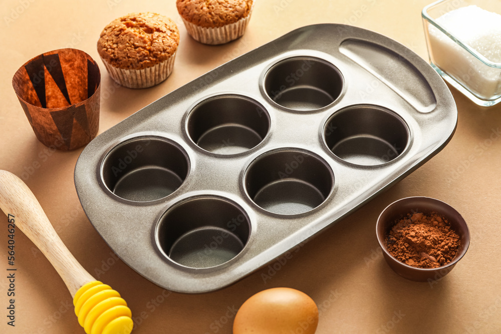 Baking tray with muffins, honey dipper and ingredients on beige background