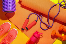 Skipping Rope With Mat, Dumbbells, Bottle And Sneakers On Color Background