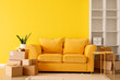 Cardboard boxes with yellow sofa, table and shelving unit in living room on moving day
