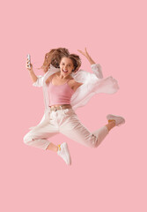Wall Mural - Young woman in earphones with mobile phone dancing on pink background