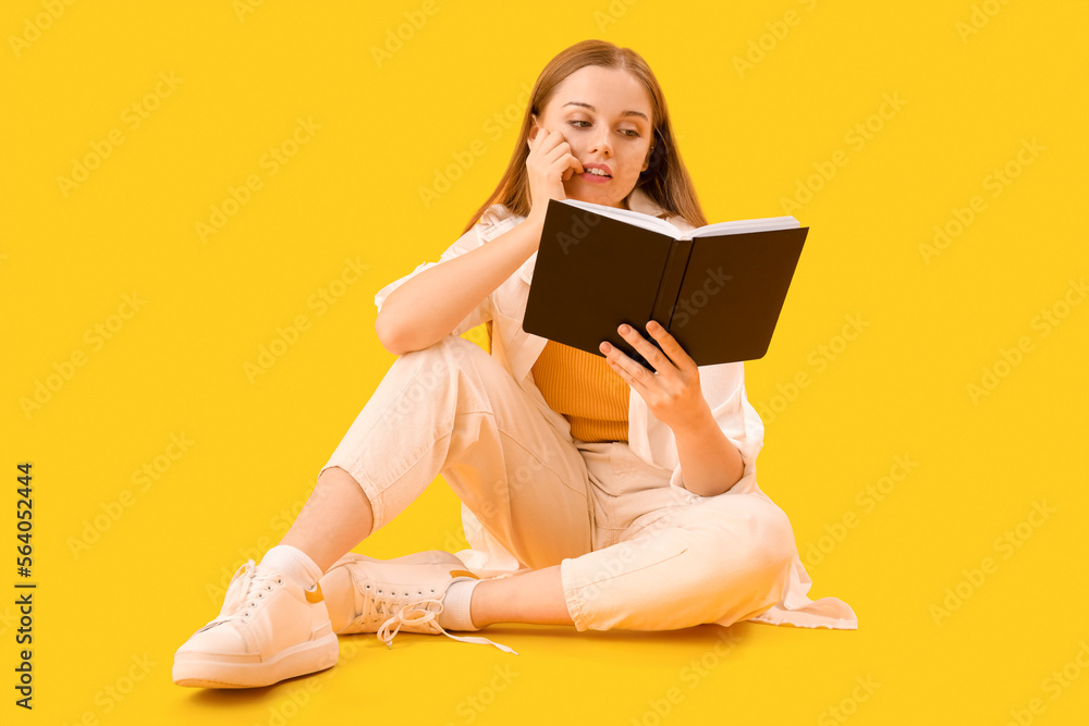 Young woman with book biting nails on yellow background