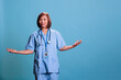 © DC Studio - Asian elderly nurse doing i don t know gesture in studio with blue background having doubt after reading patient disease expertise. Physician assistant working in health care industry