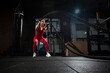 © Богдан Маліцький - young sports girl in red sportswear trains with ropes in a black dark gym, motivated woman on fitness training