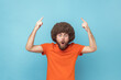 © khosrork - Wow, look, crazy advertisement. Man with Afro hairstyle in orange T-shirt pointing up at empty place for ad content and expressing astonishment. Indoor studio shot isolated on blue background.