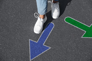 Wall Mural - Choice of way. Woman walking to drawn mark on road, closeup. Green and blue arrows pointing in different directions