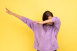 Winning, success gesture. Portrait of woman showing dab dance pose, famous internet meme, performing dabbing trends, wearing purple hoodie. Indoor studio shot isolated on yellow background.