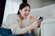 © Monster Ztudio - Happy young asian woman relax on comfortable couch at home texting messaging on smartphone, smiling girl use cellphone, browse wireless internet on gadget, shopping online from home