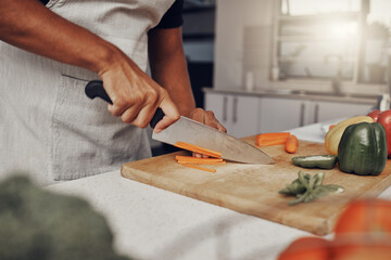 Wall Mural - Hands, food and salad with a man cooking in the kitchen, while cutting carrots on a wooden chopping board. Nutrition, health or diet with a male chef preparing a meal while standing alone in his home