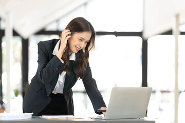 Wall Mural - Focused young businesswoman standing at table in office, using laptop, looking at computer screen, reading or writing business email, searching information in internet, working on project